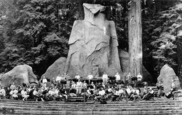 A massive mossy stone owl statue representing the legendary bohemian grove owl standing quietly under old-growth redwoods.